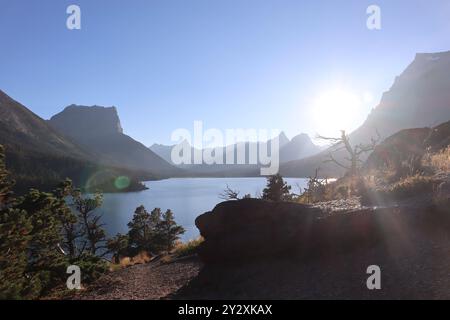 Una vista panoramica di un lago di montagna con il sole splendente sulle cime e un cielo azzurro. Foto Stock