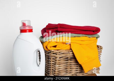 Cestello in vimini pieno di abiti vivaci e ben piegati accanto a un modello di bottiglia di detersivo per bucato. Foto Stock