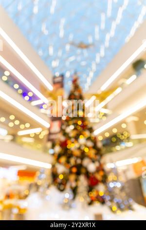 Immagine sfocata dell'albero di Natale splendidamente decorato circondato da luci festose in un centro commerciale durante le festività natalizie. Può essere utilizzato Foto Stock