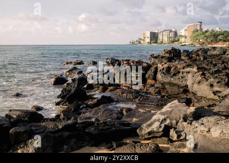 Una vista panoramica sulla costa caratterizzata da coste rocciose ed edifici in lontananza. Maui, Hawaii Foto Stock