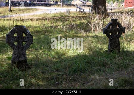 Due antiche lapidi celtiche a croce in una zona erbosa, circondate da alberi e un sentiero sullo sfondo. La luce del sole proietta ombre sul terreno, cre Foto Stock