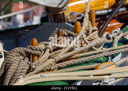 Primo piano di corde nautiche e tacche in legno su un ponte di barche, che mostra intricati nodi e dettagli marittimi. Foto Stock