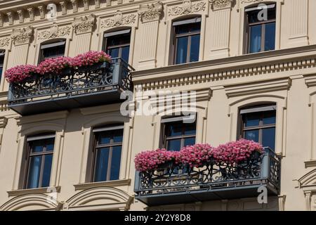 Una splendida facciata dell'edificio presenta due balconi adornati da vibranti fiori rosa. L'architettura presenta dettagli intricati e grandi finestre, Foto Stock