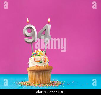 Candela di compleanno illuminata con il numero 94 - biglietto celebrazione su sfondo viola e blu Foto Stock