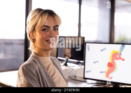 Donna sorridente in ufficio con computer che visualizza animazioni colorate ai cavallucci marini Foto Stock