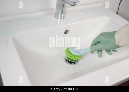 Pulizia efficace di un lavandino di carta igienica utilizzando una spugna e indossando guanti per la massima protezione Foto Stock