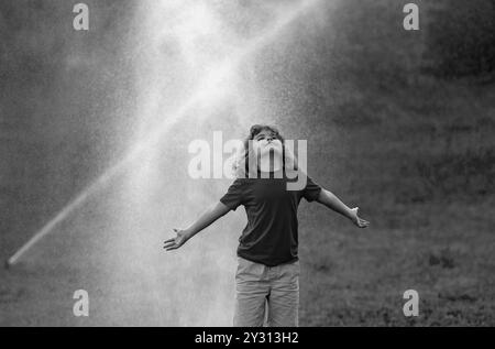 I bambini giocano in giardino. Bambini vicino a irroratrici automatiche in giardino. Innaffiare in giardino. Irrigatore automatico per prati che innaffia l'erba. Sistema di irrigazione del giardino Foto Stock