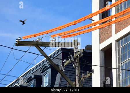 Coperture per linee elettriche, protezioni per linee di sicurezza arancioni che coprono i cavi elettrici su un palo di pubblica utilità vicino a un cantiere edile per la sicurezza dei lavoratori Foto Stock