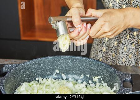 Per aggiungere aglio fresco in una padella ripiena di cipolle tritate, viene utilizzata una pressa all'aglio. Foto Stock