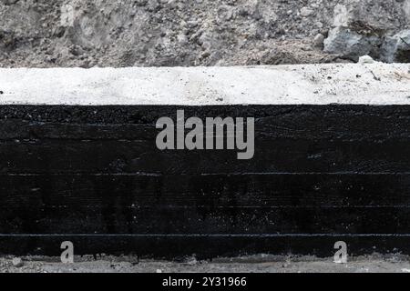 La parete di fondazione in cemento armato è rivestita con una composizione bituminosa nera protettiva, vista frontale Foto Stock