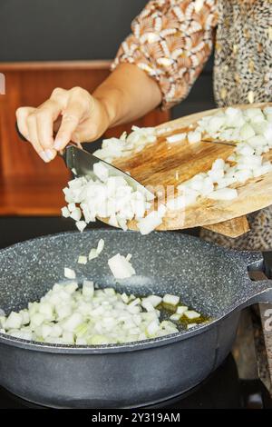 Le cipolle tritate vengono trasferite da un bordo di legno in una padella con olio per la cottura. Foto Stock