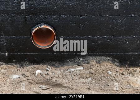 Il tubo di scarico è montato su una parete di fondazione in cemento armato rivestita con una composizione bituminosa nera protettiva, vista frontale Foto Stock