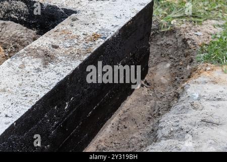 Le fondamenta a strisce in cemento armato sono rivestite con una composizione bituminosa nera protettiva, la casa rurale è in costruzione Foto Stock