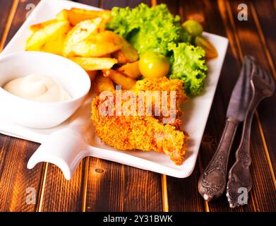 Deliziose ali di pollo fritte accompagnate da spicchi di patate dorate servite con salsa cremosa su piatto bianco Foto Stock