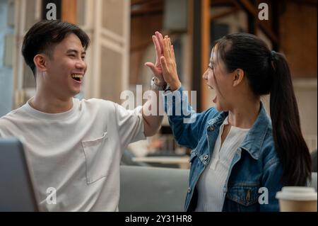 Due giovani amici asiatici allegri ed eccitati festeggiano insieme buone notizie, dandoci a vicenda cinque con espressioni felicissime. lavoro di squadra, f Foto Stock