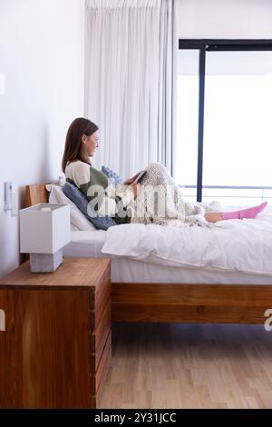 A casa, rilassarsi a letto, donna che legge un libro e godersi il tempo libero Foto Stock