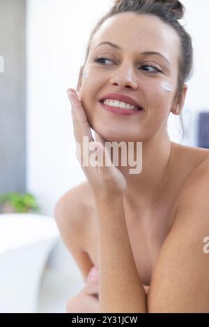 A casa, applicando crema viso, giovane donna sorridente e godendo di trattamenti spa Foto Stock