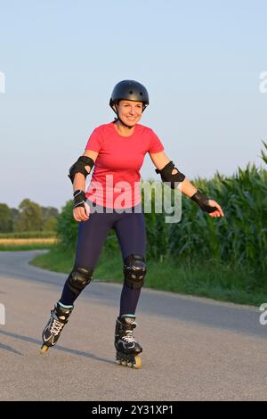 Giovane donna che indossa protezioni e casco rollerblade su una piccola strada. Foto Stock