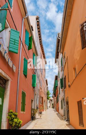 Si può passeggiare per le strade storiche di Rovigno, dove i vivaci edifici arancioni e verdi fiancheggiano lo stretto sentiero, bagnati dalla calda luce del sole Foto Stock