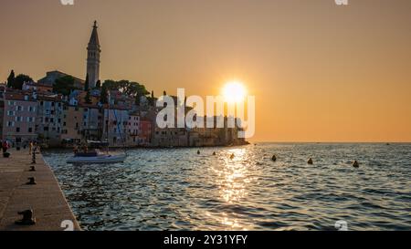 Mentre il sole tramonta su Rovigno, Croazia, la sua calda luce illumina gli edifici color pastello lungo la costa. Le barche si arrampicano dolcemente nel tranquillo wat Foto Stock