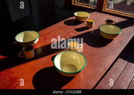 vecchie tazze e ciotole smaltate sul tavolo sotto la luce del sole all'interno Foto Stock