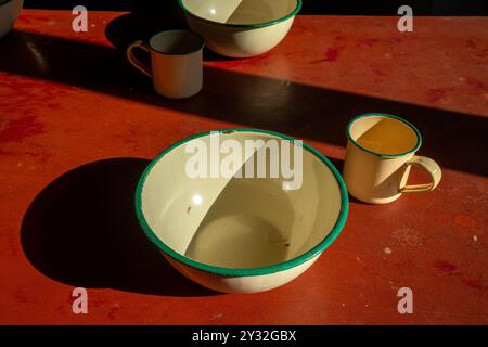 vecchie tazze e ciotole smaltate sul tavolo sotto la luce del sole all'interno Foto Stock