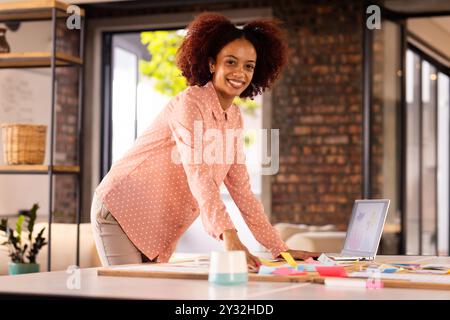 Donna sorridente che organizza appunti colorati sulla scrivania nell'ufficio creativo Foto Stock