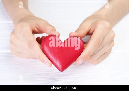 Donna che tiene il cuore rosso al tavolo di legno bianco, primo piano Foto Stock