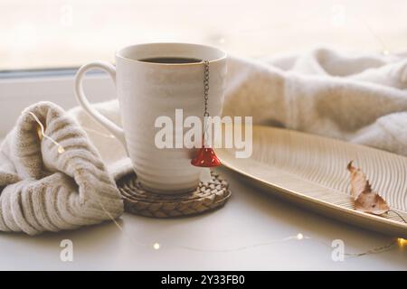 Accogliente allestimento autunnale con una tazza di tè fumante e arredi per la casa Foto Stock