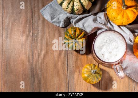 Buia di zucca spumosa in tazza di vetro di birra, bevanda alcolica fatta in casa autunno, con piccole zucche su tavolo da cucina in legno Foto Stock