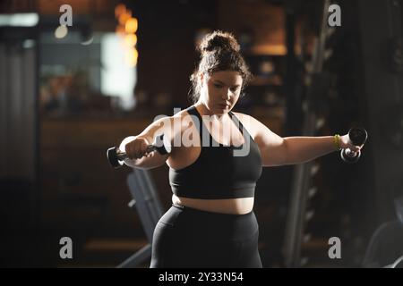 Una giovane donna determinata solleva pesi in abbigliamento sportivo, celebrando la forza e la positività del corpo in palestra. Foto Stock