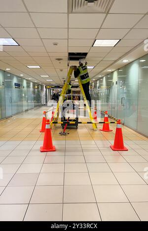 Un uomo con un giubbotto giallo è su una scala in un corridoio. Ci sono coni arancioni sul pavimento, l'aeroporto internazionale Jorge Chavez Foto Stock