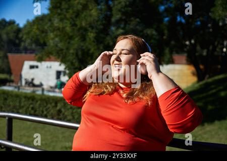 Una donna di grandi dimensioni si rilassa ed esercita all'aperto, immersa nella sua musica. Foto Stock