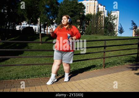 Una donna dalle dimensioni più grandi e vibranti si esercita mentre ascolta musica all'aperto. Foto Stock