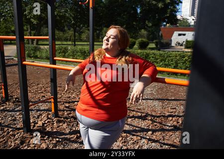 Una donna di grandi dimensioni si esercita all'aperto, immergendosi nel sole in un parco vivace. Foto Stock