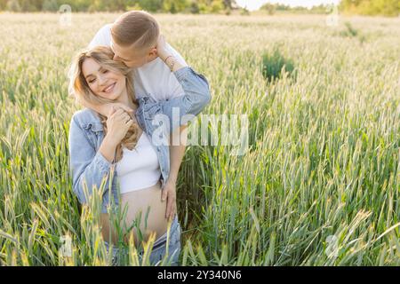 L'uomo porta con gioia la donna incinta attraverso il campo di grano in un paesaggio naturale Foto Stock