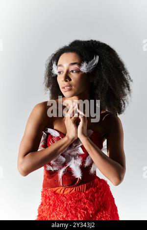 Una giovane donna graziosa si posa elegantemente in un sorprendente ensemble rosso adornato di piume. Foto Stock