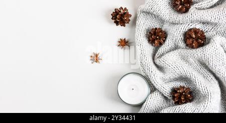 Accogliente sfondo grigio inverno realizzato con coperta a maglia, candela bianca, coni e anice stellato con spazio per testo e saluti. Concetto di atmosfera familiare calda e accogliente Foto Stock