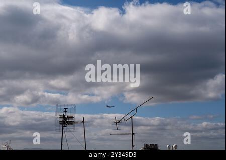 Un jet da caccia vola attraverso un cielo frastagliato, incorniciato da antenne arrugginite sul tetto Foto Stock