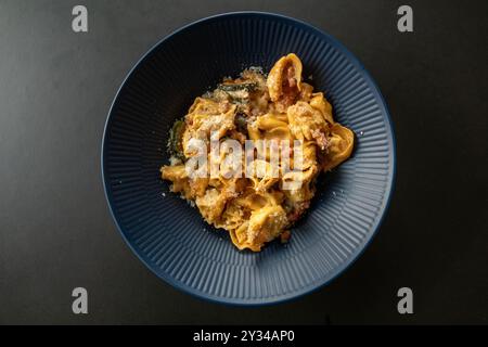 Piatto di Tortellini ripieno di pasta con salsa e cosparso di parmigiano Reggiano. Vista dall'alto con sfondo nero rustico. Foto Stock