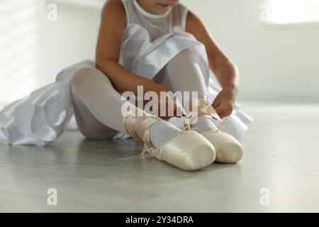 Piccola ballerina che lega le scarpe pointe all'interno, primo piano Foto Stock