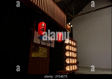 Ambiente interno minimalista caratterizzato da un allestimento in stile giapponese con lanterne rosse e lanterne di carta bianca disposte in modo ordinato Foto Stock