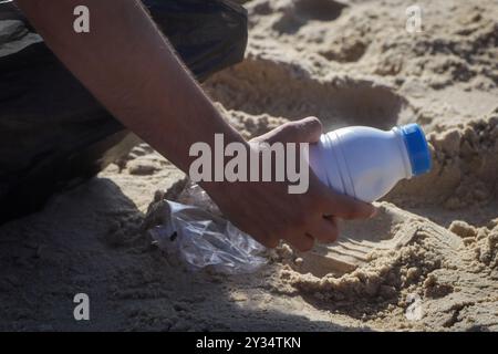 Mano Tan di un uomo che raccoglie spazzatura su una bellissima spiaggia di sabbia dorata in una borsa nera Foto Stock