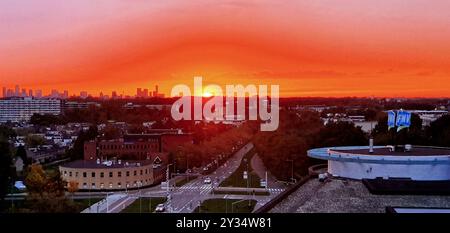 Uno splendido tramonto sullo skyline della città, con vivaci sfumature arancione e rosso che riempiono il cielo. Il sole sta tramontando all'orizzonte, proiettando un caldo bagliore su t Foto Stock