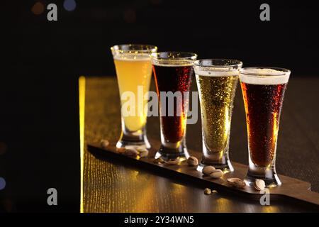 Bicchieri con diversi tipi di birra e pistacchi su un tavolo di legno su sfondo nero, primo piano. Spazio per il testo Foto Stock