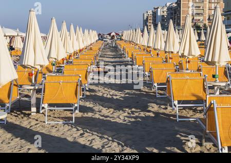 Righe di colore arancione di ombrelloni e sdraio sulla spiaggia di Igea Marina vicino a Rimini Foto Stock