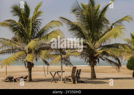 Due sedie e tavolino sotto una foglia di palma e ombrellone in legno sulla spiaggia di Bijilo in Gambia Foto Stock