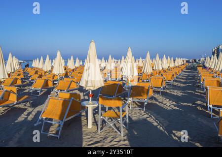 Righe di colore arancione di ombrelloni e sdraio sulla spiaggia di Igea Marina vicino a Rimini Foto Stock