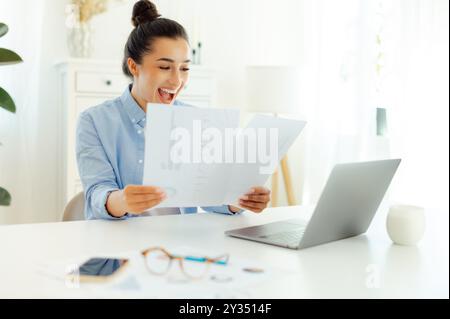 Felice felice felice felice eccitata donna d'affari di successo indiana o araba seduta sul posto di lavoro, analizzando documenti finanziari, gioendo del successo, buoni risultati di lavoro, sorridendo Foto Stock