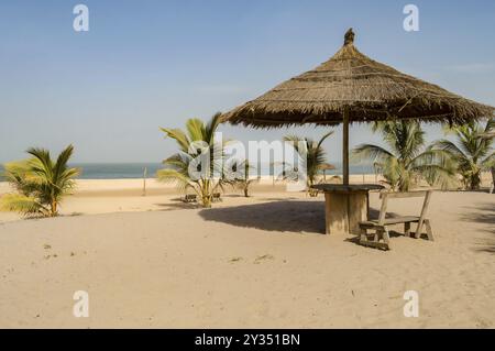 Ombrellone in paglia con piccola panca in legno e tavolo sulla spiaggia di Bijilo in Gambia Foto Stock